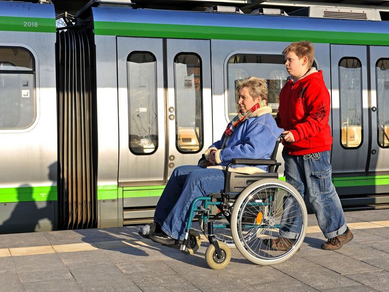 Frau im Rollstuhl mit Begleitung auf Bahnsteig